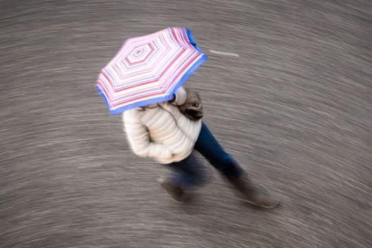 Eine Frau geht bei regnerischem Wetter über eine Straße (Symbolbild): Am Wochenende wird es an einem Tag deutlich frischer, auch die Nächte werden kalt.