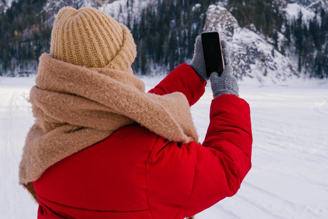 Eine Frau mit Smartphone im Winter (Symbolbild): Bei Kälte verhalten sich Smartphones plötzlich anders – warum eigentlich?