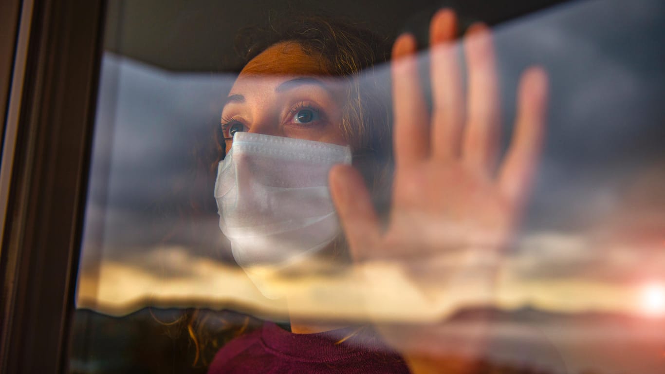 Eine Frau mit Maske guckt aus dem Fenster