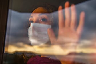 Eine Frau mit Maske guckt aus dem Fenster