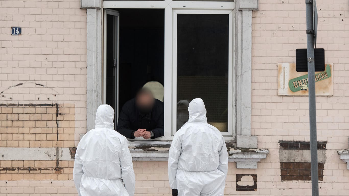 Einsatzkräfte der Polizei unterhalten sich durch ein Fenster mit einem Mann: Vier Wohnhäuser stehen unter Quarantäne.