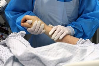 Im Infektionszimmer hält die Mitarbeiterin einer Intensivstation die Hand eines Covid-19-Patienten: Laut dem Chef-Pathologen der Uniklinik Augsburg sind die meisten Corona-Toten an und nicht mit dem Virus gestorben.