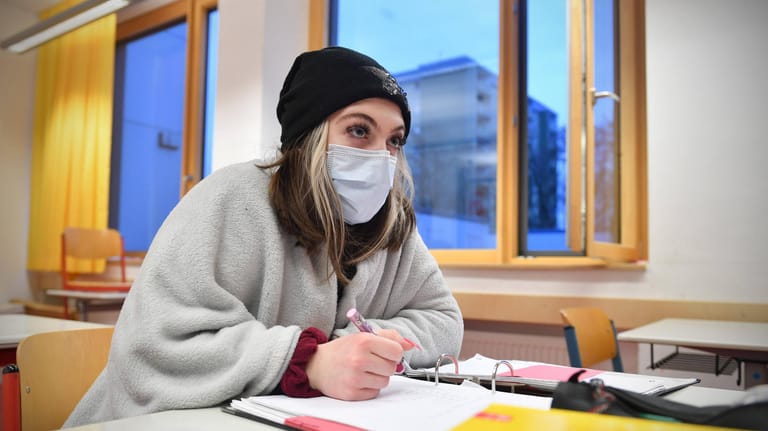 Eine Schülerin sitzt mit Mund-Nasen-Schutz und bei geöffnetem Fenster im Klassenzimmer (Symbolbild): Kölner Eltern setzen sich für die Anschaffung von Luftfilteranlagen in Schulen ein.