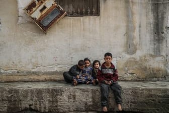 Syrische Kinder sitzen zwischen beschädigten Gebäuden im Dorf Afes.