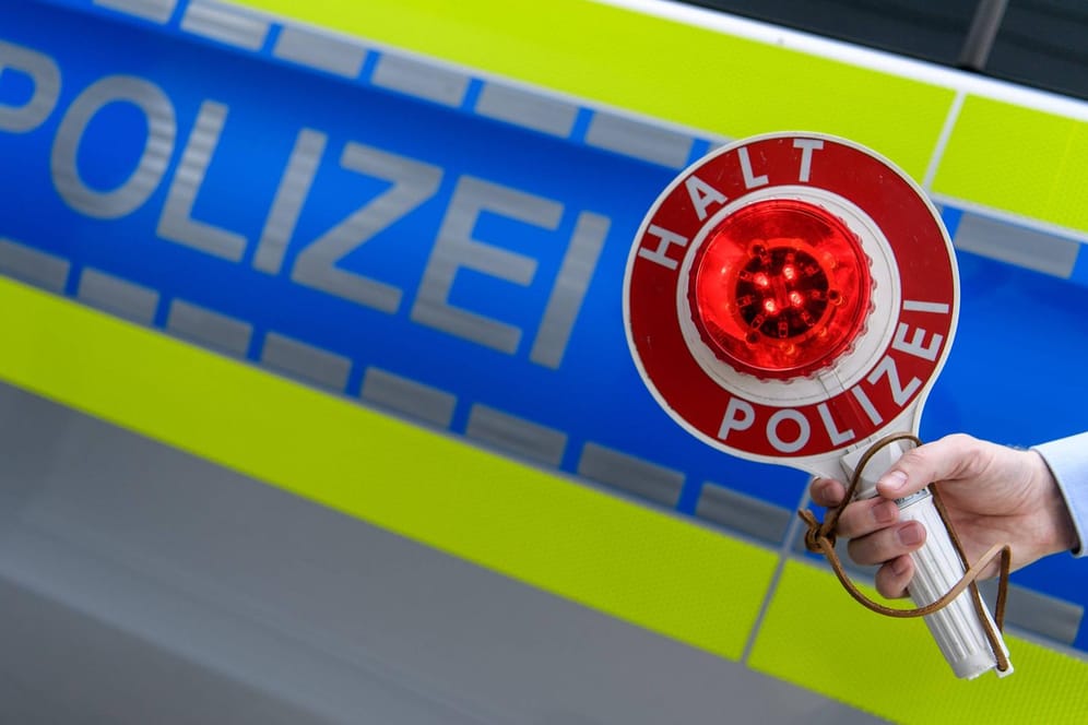Eine Person hält eine "Stopp"-Kelle vor einem Polizei-Auto (Symboldbild): Auf der A3 bei Bonn haben sich zwei Männer als Polizisten ausgegeben und bei einer Kontrolle mehrere Tausend Euro erbeutet.