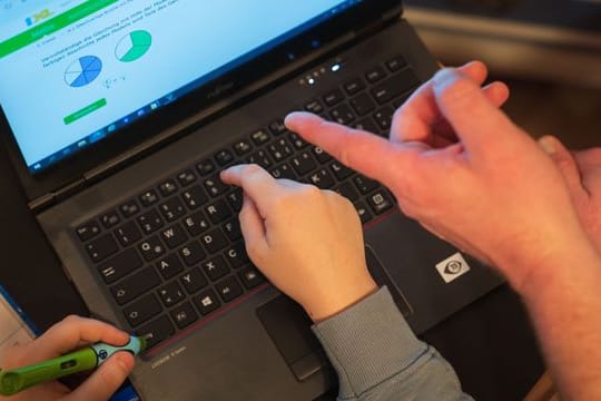 Ein Junge nutzt zusammen mit seinem Vater einen Laptop für den Heimunterricht.