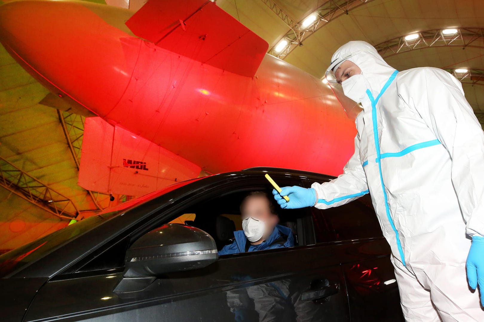 Im Luftschiffhangar des Flughafens Essen/Mülheim führt ein Rote Kreuz-Mitarbeiter im Drive-In-Testzentrum einen Corona-Schnelltest durch.