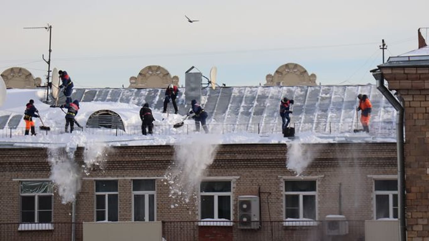 Menschen schaufeln Schnee vom Dach eines Mehrfamilienhauses in Moskau.