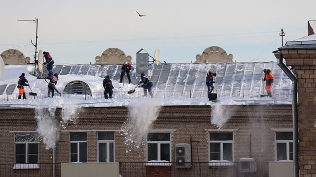 Menschen schaufeln Schnee vom Dach eines Mehrfamilienhauses in Moskau. Menschen schaufeln Schnee vom Dach eines Mehrfamilienhauses in Moskau.
