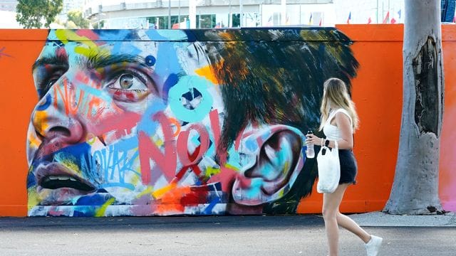 Eine Frau geht an einem Wandbild von Novak Djokovic vorbei, das auf eine Wand im Melbourne Park gemalt wurde. Eine Frau geht an einem Wandbild von Novak Djokovic vorbei, das auf eine Wand im Melbourne Park gemalt wurde.