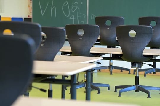 In einem leeren Klassenzimmer sind die Stühle auf die Schulbänke gestellt.