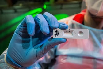 Ein Labormitarbeiter zeigt einen Schnelltest. Die auf PCR-Tests basierenden Zahlen der Gesundheitsämter sind leicht gesunken, der Inzidenzwert steigt aber.