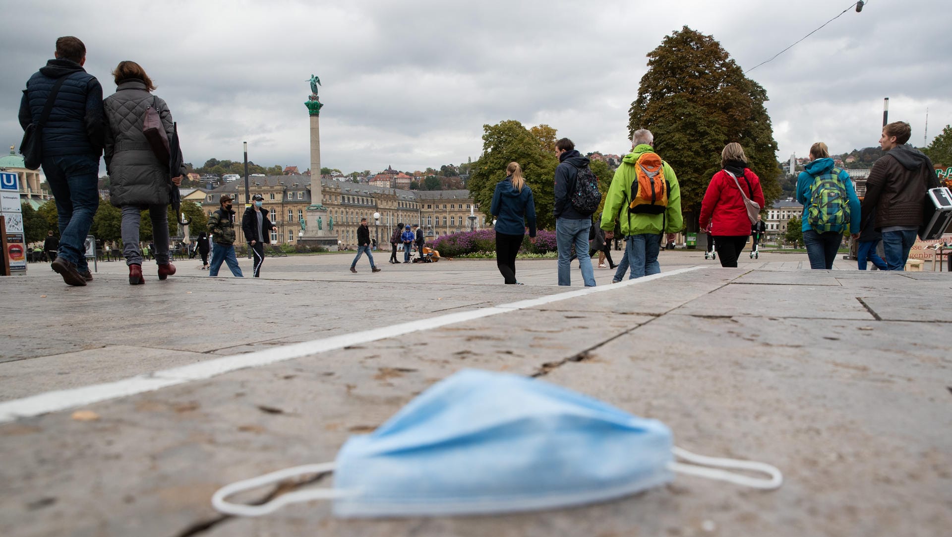 Stuttgart: Passanten gehen über den Schlossplatz, während auf dem Boden eine Mund-Nasen-Bedeckung liegt.