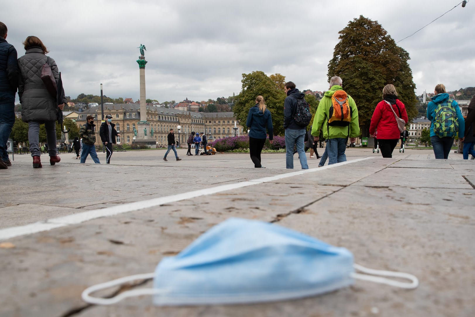 Stuttgart: Passanten gehen über den Schlossplatz, während auf dem Boden eine Mund-Nasen-Bedeckung liegt.