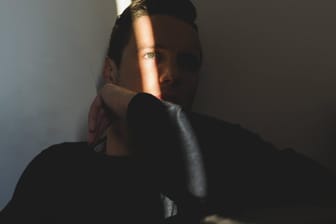 Ein Mann sitzt in seiner abgedunkelten Wohnung und schaut ins Freie (Symbolbild): Für psychisch Erkrankte können die Belastungen des Corona-Lockdowns traumatisch sein.