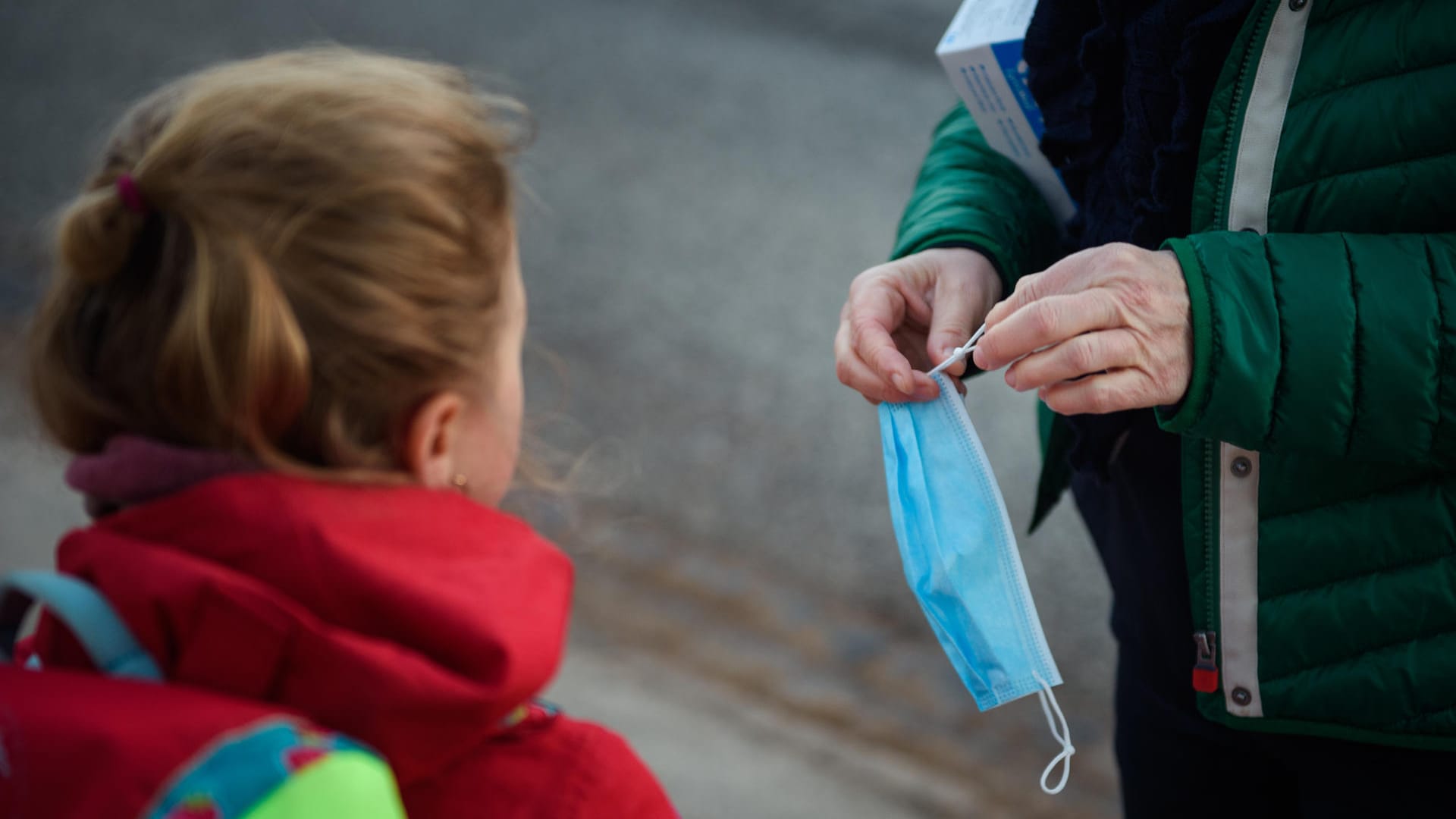 Eine Lehrerin kürzt einen Mund-Nasen-Schutz für eine Schülerin (Symbolbild): Für einen Teil der Schüler ging es am Montag zurück in die Schulen.