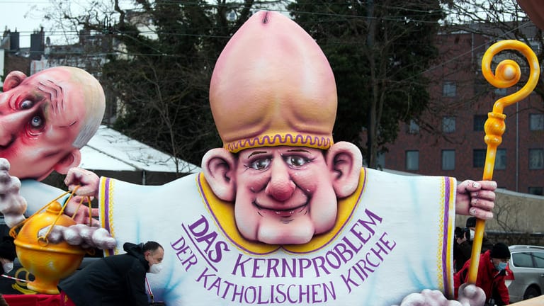 Karnevalswagen mit einem Priester, der eine Eichel als Hut trägt und auf dem Gewand die Aufschrift "Das Kernproblem der katholischen Kirche" trägt: Viele Menschen vertrauen besonders der katholischen Kirche nicht.