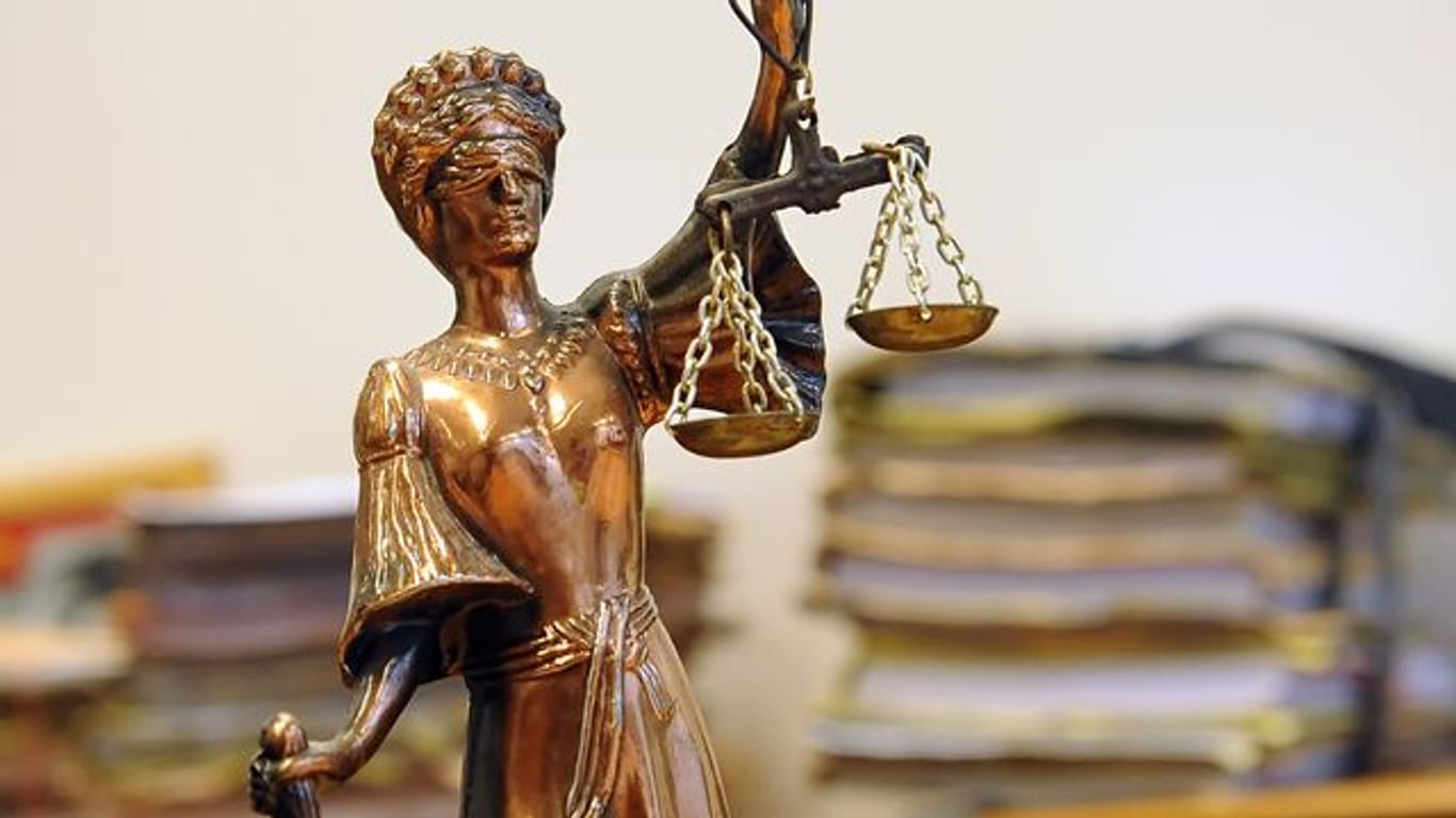 Eine goldfarbene Justitia-Figur steht vor Aktenbergen, die sich auf einem Tisch stapeln (Symbolbild): In Hagen ist ein Mann wegen der Tötung seiner Freundin verurteilt worden.