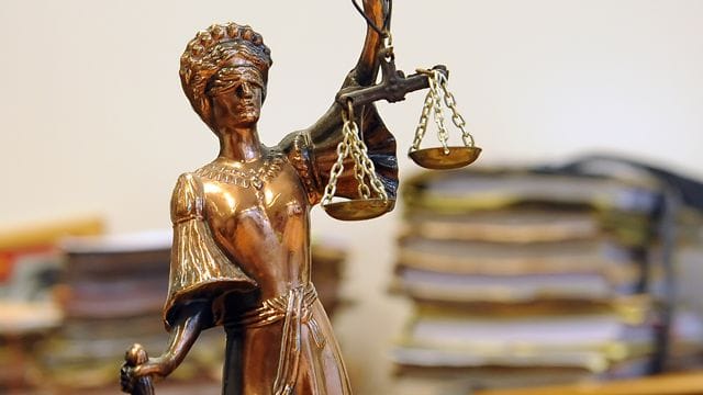 Eine goldfarbene Justitia-Figur steht vor Aktenbergen, die sich auf einem Tisch stapeln (Symbolbild): In Hagen ist ein Mann wegen der Tötung seiner Freundin verurteilt worden.