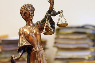 Eine goldfarbene Justitia-Figur steht vor Aktenbergen, die sich auf einem Tisch stapeln (Symbolbild): In Hagen ist ein Mann wegen der Tötung seiner Freundin verurteilt worden.