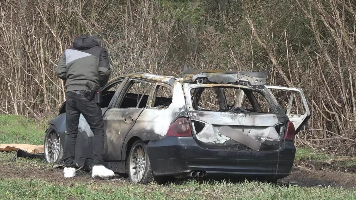 März 2018: Ein Polizeibeamter steht neben einem ausgebrannten Auto, das zwei Männer nach einem Überfall auf einen Geldtransporter zur Flucht genutzt haben sollen.