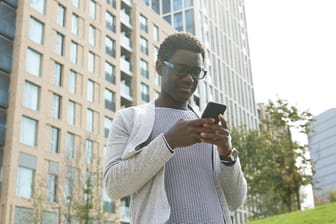 Junger Mann mit Smartphone (Symbolbild): Eine Auswertung zeigt, wie viel man in Deutschlands größten Städten verdient.