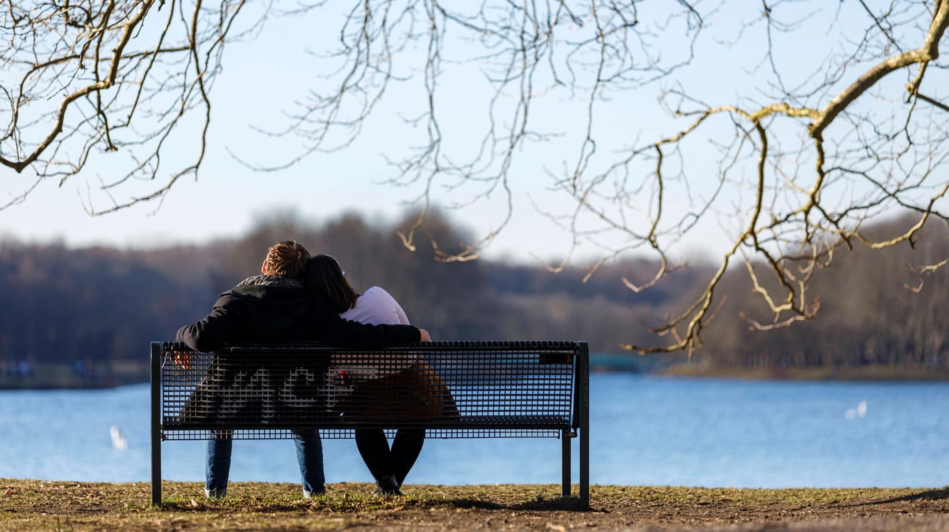 Ein Paar sitzt auf einer Bank am Decksteiner Weiher (Archivbild): So frühlingshaft wird das Wetter am Wochenende nicht mehr aussehen.