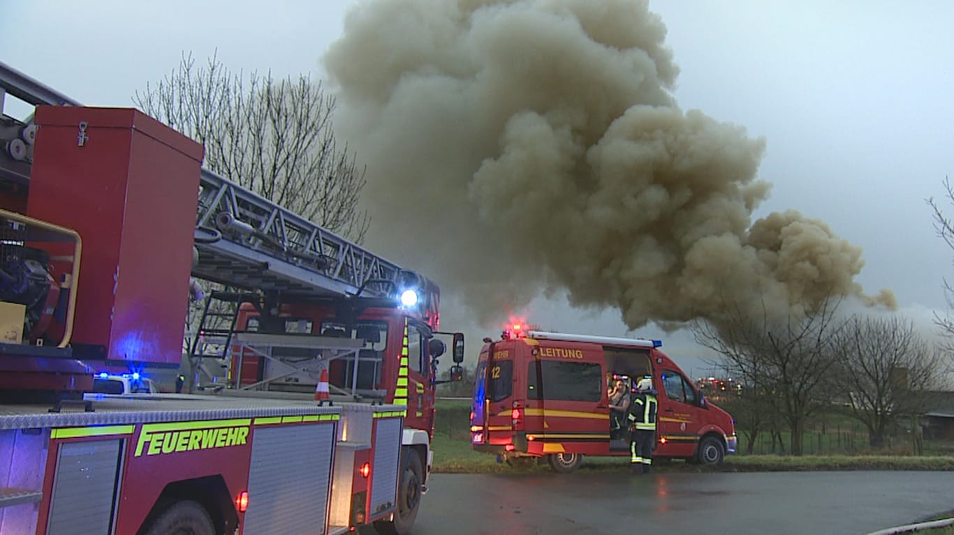 Nordrhein-Westfalen, Kerken: Einsatzkräfte der Feuerwehr stehen vor der hohen Rauchwolke eines brennenden Schweinestalls.