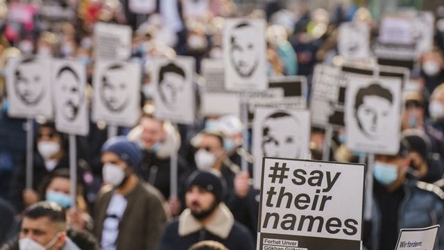 Ein Plakat mit der Aufschrift "#say their names" wird auf einer Kundgebung zum Gedenken an den rassistischen Anschlag in Hanau hochgehalten. Ein Plakat mit der Aufschrift "#say their names" wird auf einer Kundgebung zum Gedenken an den rassistischen Anschlag in Hanau hochgehalten.