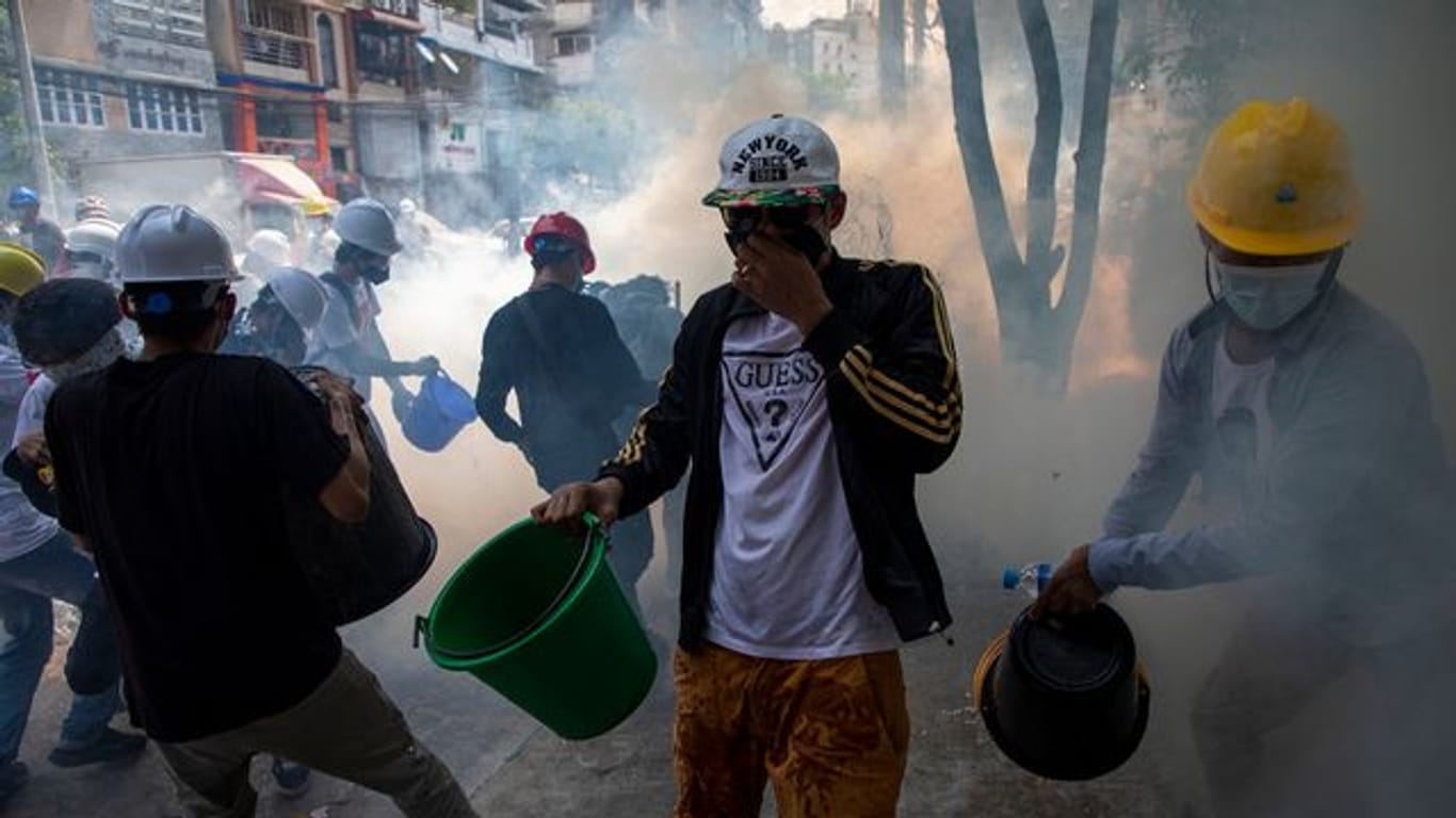 Demonstranten mit Helmen und Mund-Nasen-Schutz versuchen, rauchende Tränengaskanister mit Wasser zu löschen.