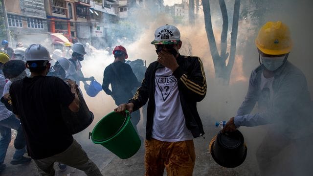 Demonstranten mit Helmen und Mund-Nasen-Schutz versuchen, rauchende Tränengaskanister mit Wasser zu löschen. Demonstranten mit Helmen und Mund-Nasen-Schutz versuchen, rauchende Tränengaskanister mit Wasser zu löschen.