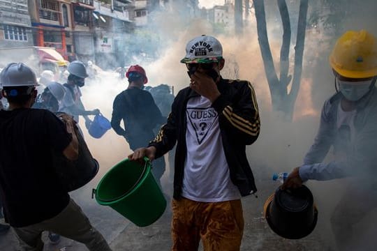 Demonstranten mit Helmen und Mund-Nasen-Schutz versuchen, rauchende Tränengaskanister mit Wasser zu löschen.