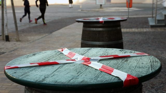 Kein gemütliches Beisammensein: Mit einem rot-weißen-Flatterband sind Stehtische an der Promenade des Ostseebades Warnemünde abgeklebt.