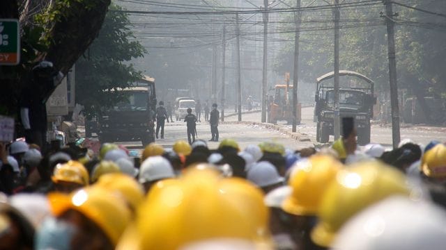 Demonstranten in Mandalay tragen gelbe Schutzhelme und beobachten auf einer blockierten Straße die Polizei. Demonstranten in Mandalay tragen gelbe Schutzhelme und beobachten auf einer blockierten Straße die Polizei.