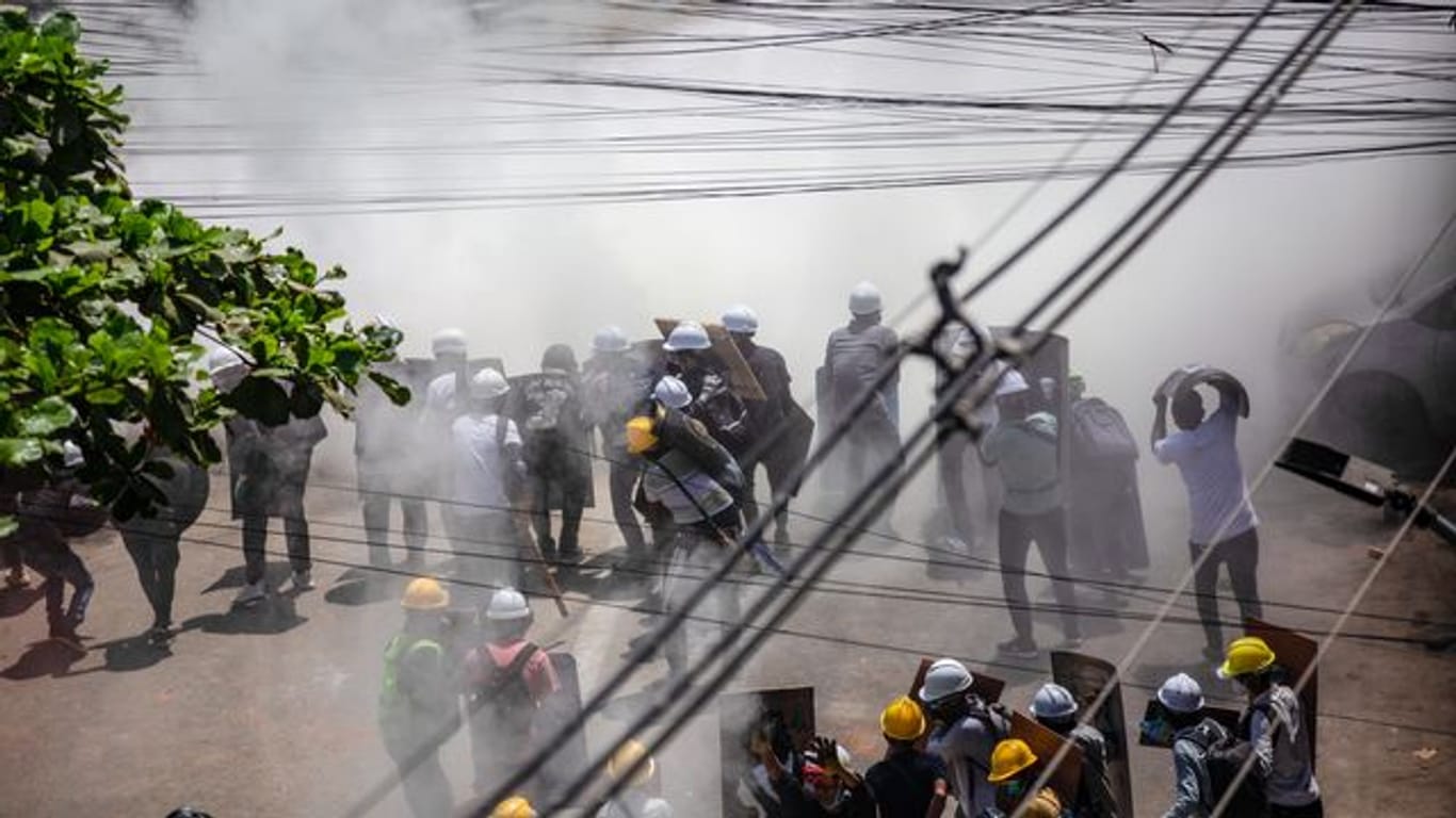Demonstranten tragen in Rangun in einer Wolke von Tränengas Schutzhelme, um sich gegen die Gewalt zu schützen.