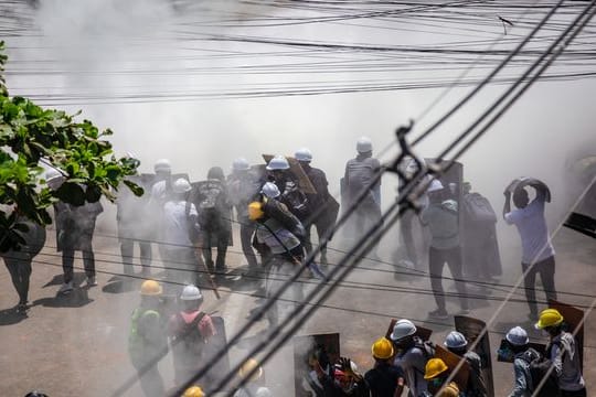 Demonstranten tragen in Rangun in einer Wolke von Tränengas Schutzhelme, um sich gegen die Gewalt zu schützen.