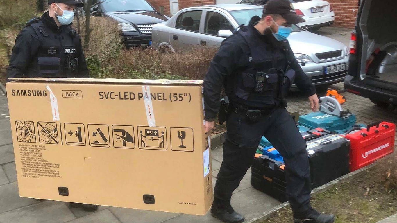 Zwei Polizisten tragen einen verpackten Fernseher: Auch zahlreiche Werkzeugkoffer konnten in den Wohnungen der Verdächtigen gefunden werden.