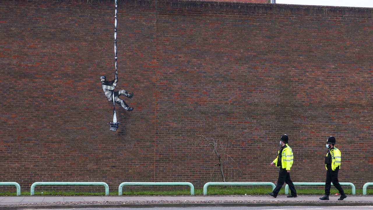 Polizisten gehen vor einem Wandgemälde des Streetart-Künstlers Banksy an der Mauer eines ehemaligen Gefängnisses. Polizisten gehen vor einem Wandgemälde des Streetart-Künstlers Banksy an der Mauer eines ehemaligen Gefängnisses.
