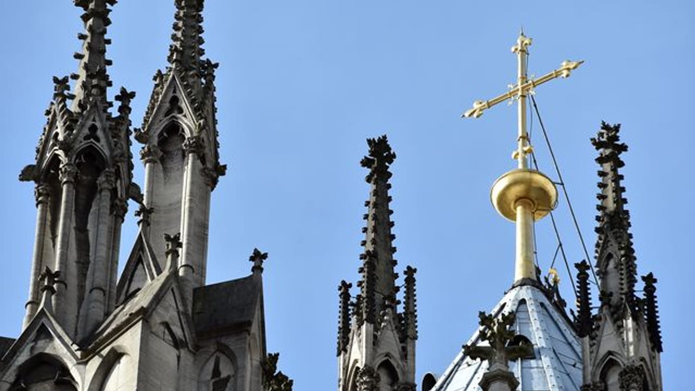 Ein goldenes Kreuz auf dem Kölner Dom (Archivbild): Der Kölner Erzbischof will ein umstrittenes Gutachten veröffentlichen.
