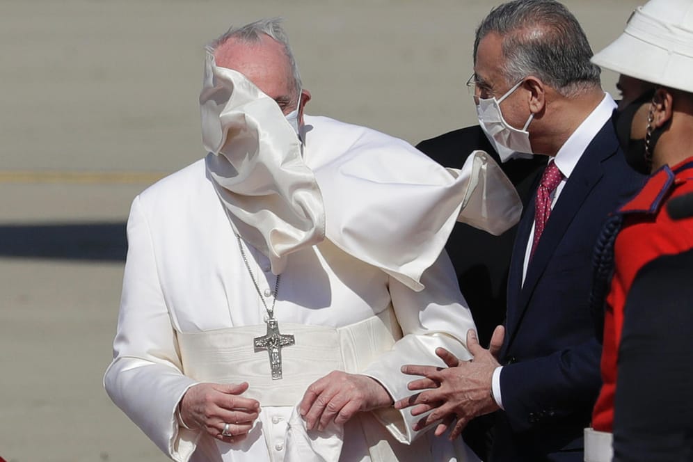 Auf dem Flughafen in Bagdad: Papst Franziskus wird von Premier Mustafa al-Kadhimi empfangen. Der Wind weht ihm die Mozzetta ins Gesicht.