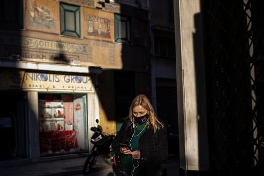 Eine Frau, die eine schützende Gesichtsmaske trägt, geht im Zentrum von Athen.