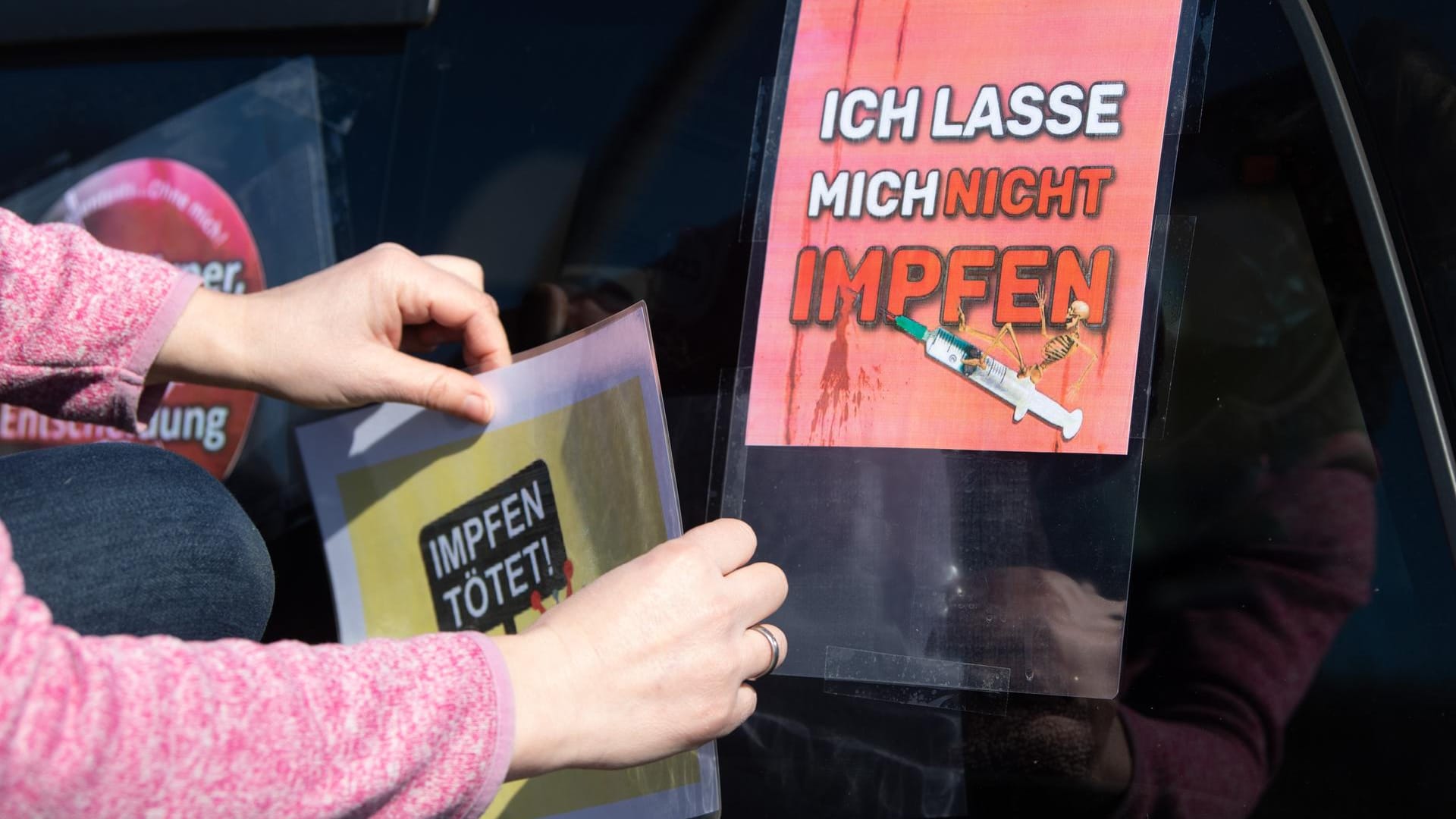 Eine Teilnehmerin eines Autokorsos klebt auf einem Parkplatz an der Autobahn 4 ein Schild mit der Aufschrift "Impfen tötet" auf die Heckscheibe eines Fahrzeugs: An den Protest-Korsos beteiligten sich deutlich weniger Menschen als erwartet.