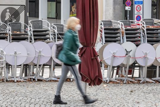 Eine Frau geht an zusammengestellten Tischen und Stühlen eines Cafes in der Innenstadt vorbei (Symbolbild): Ab Montag gelten in Bayern neue Corona-Regeln.