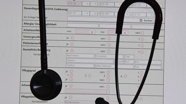 In einem Behandlungszimmer einer Praxis hängt ein Stethoskop vor einer auf einem Bildschirm dargestellten elektronischen Patientenakte (ePA). In einem Behandlungszimmer einer Praxis hängt ein Stethoskop vor einer auf einem Bildschirm dargestellten elektronischen Patientenakte (ePA).