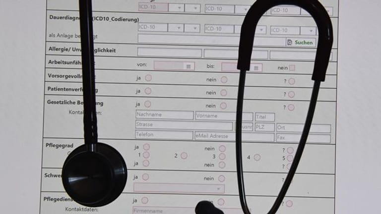 In einem Behandlungszimmer einer Praxis hängt ein Stethoskop vor einer auf einem Bildschirm dargestellten elektronischen Patientenakte (ePA).