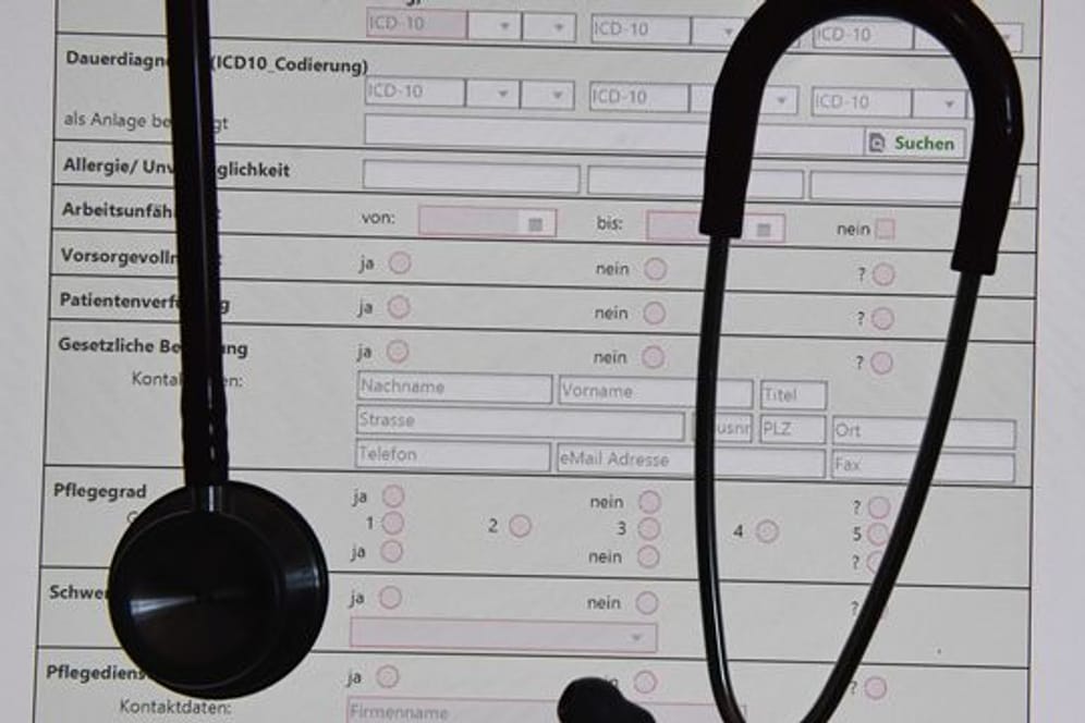 In einem Behandlungszimmer einer Praxis hängt ein Stethoskop vor einer auf einem Bildschirm dargestellten elektronischen Patientenakte (ePA).
