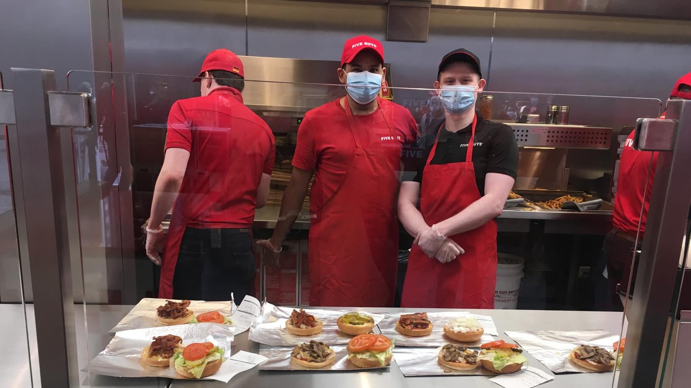 Mitarbeiter von Five Guys mit Mundschutz und hinter einer Schutzscheibe: Die Firma wirbt damit, dass keine Burger warmgehalten, sondern alle frisch zubereitet werden.