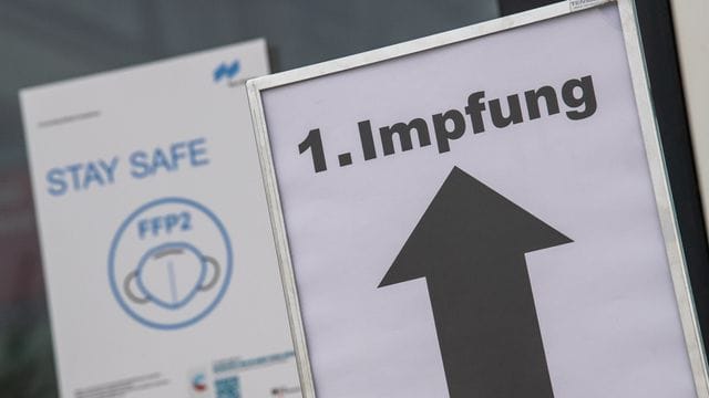 Ein Schild auf einem Messegelände weist den Weg zu einem Impfzentrum.