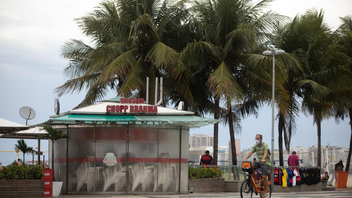 Ein Mann fährt mit dem Rad an einem geschlossenen Kiosk an den sonst gut besuchten brasilianischen Strand Copacabana: Bars und Restaurants müssen hier um 17 Uhr schließen.