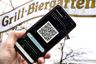 Die Luca-App mit QR-Code auf einem Smartphone vor einem Biergarten-Schild (Symbolbild): Die App könnte eine digitale und einheitliche Lösung der Kontaktnachverfolgung sein.